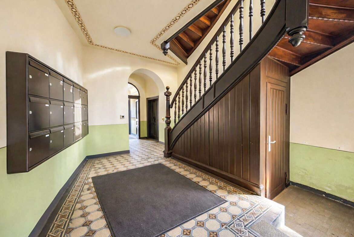 Lobby hallway with a row of mailboxes on the left, a curved dark wood staircase on the right, and green wainscoted walls.