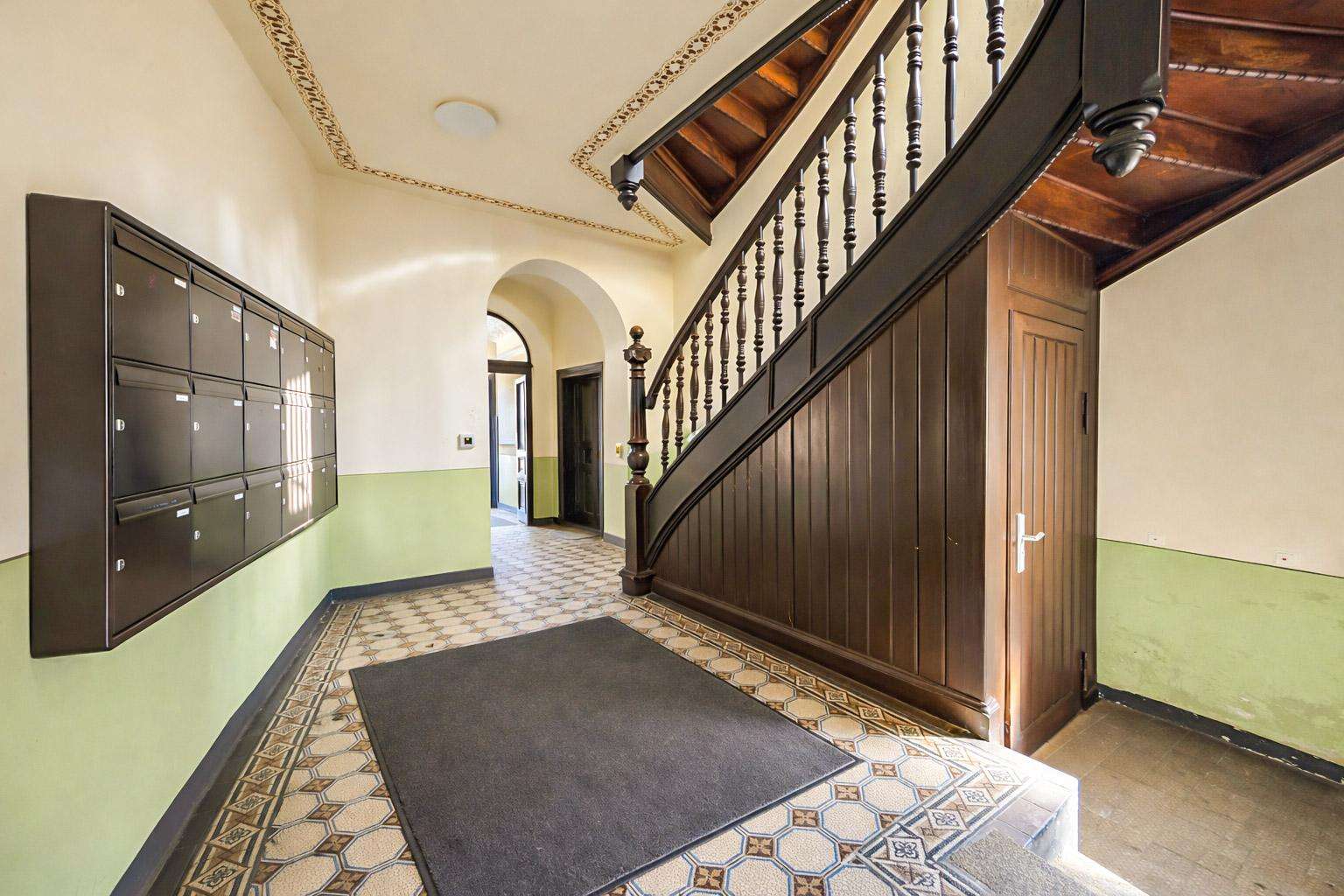 Lobby hallway with a row of mailboxes on the left, a curved dark wood staircase on the right, and green wainscoted walls.