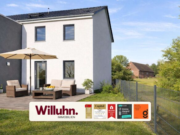 Modern white two-story house with a wooden deck, beige outdoor furniture, and a large umbrella; foreground shows a Willuhn Immobilien banner.