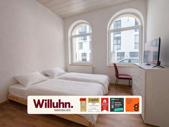 Bright apartment bedroom with two single beds, white bedding, a white dresser with a flat-screen TV, and a red chair by large arched windows.
