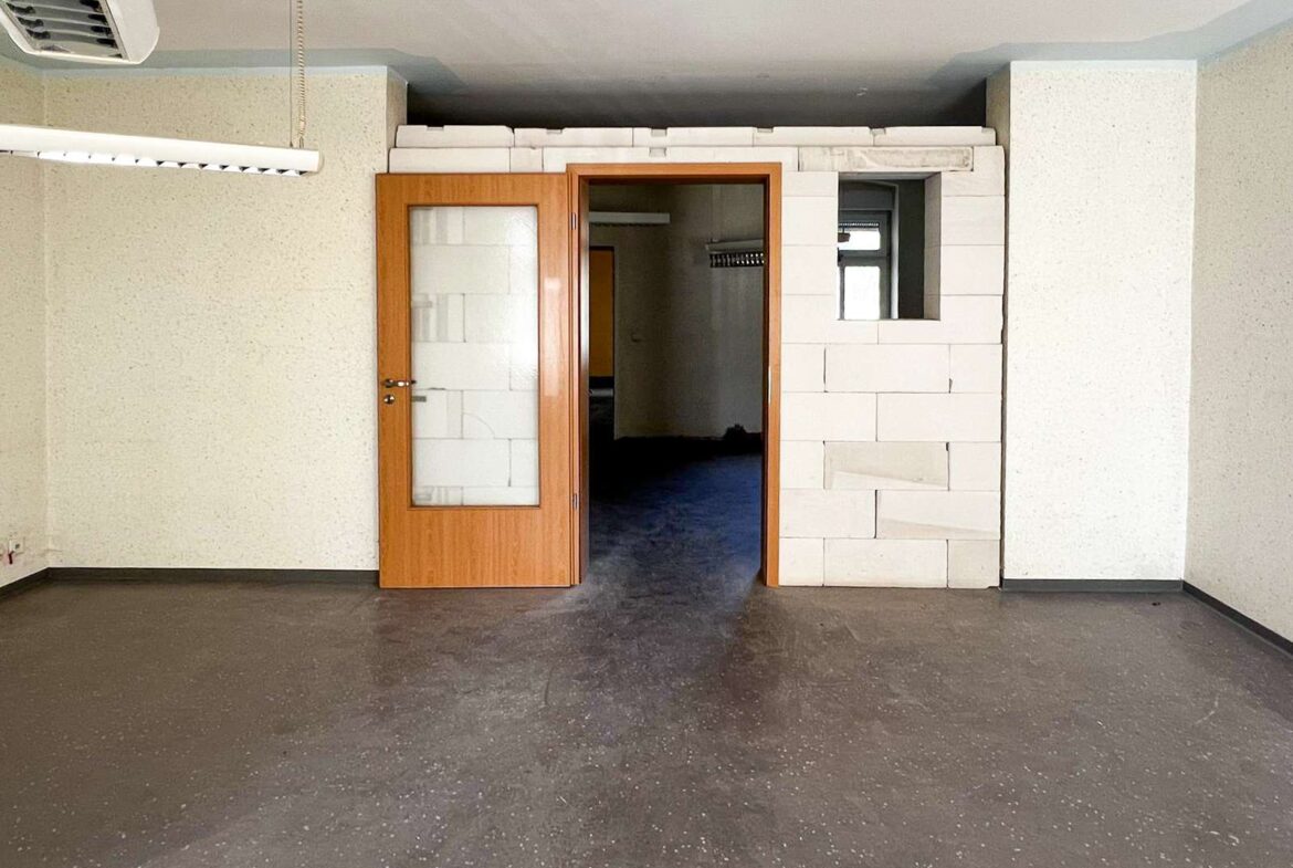 Empty industrial room with an open wooden door, white block wall sections, and a ceiling fluorescent light.