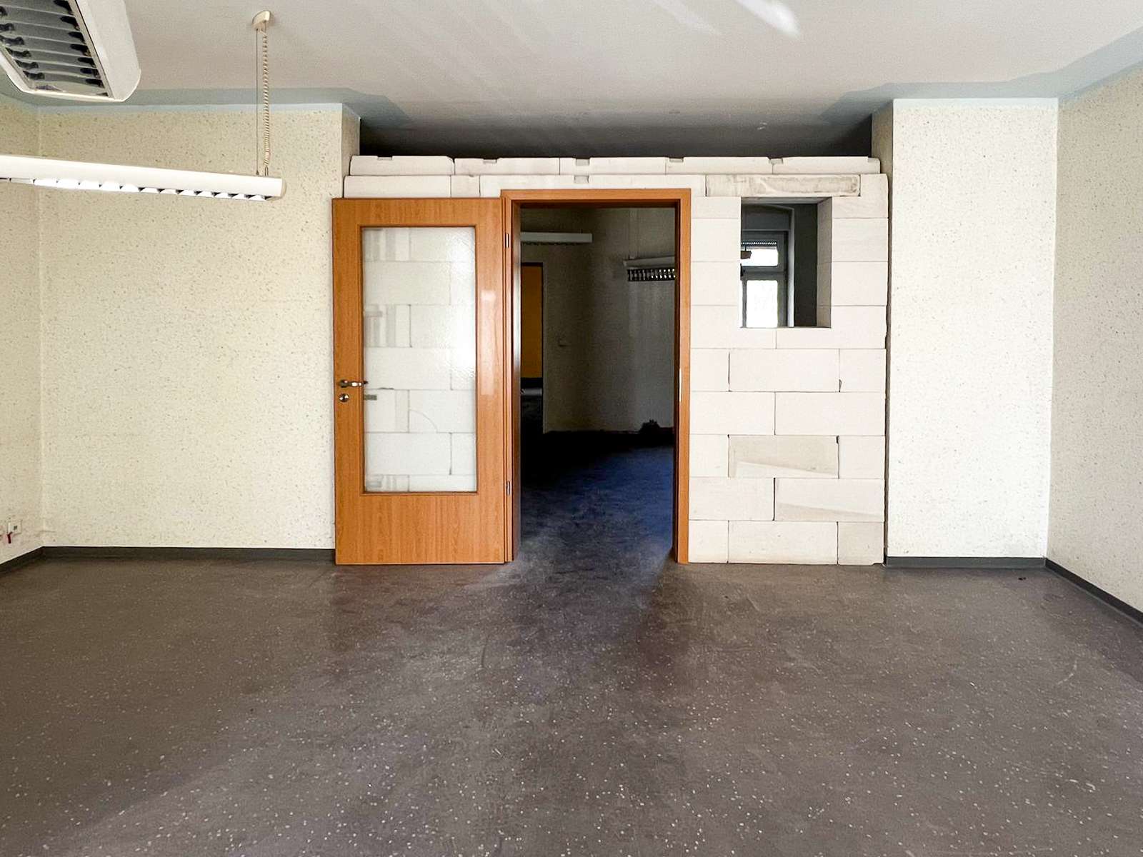 Empty industrial room with an open wooden door, white block wall sections, and a ceiling fluorescent light.