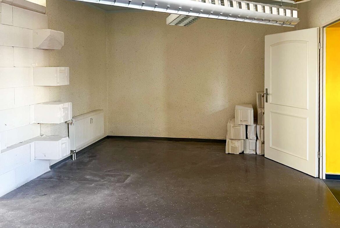 A small empty storage room with white stacked blocks along the left wall and a radiator beneath them, an open door on the right, and a pile of white blocks by the door.