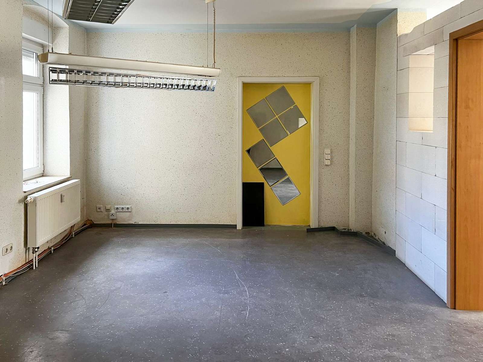Empty unfinished room with a yellow door featuring diagonal reflective panels as wall art.