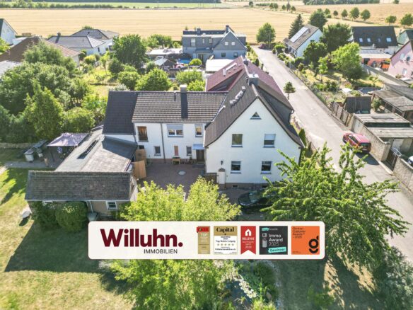 Aerial view of a suburban neighborhood with white houses, red-tiled roofs, and plenty of trees; a large Willuhn Immobilien banner runs across the bottom edge.