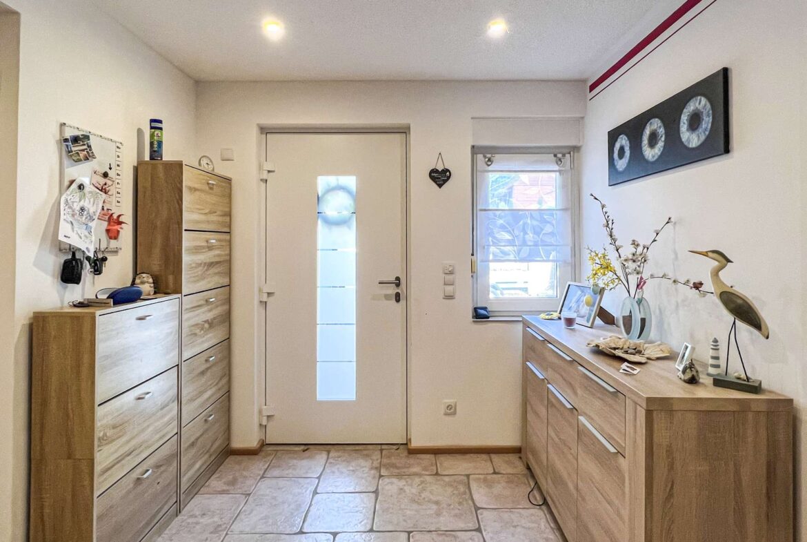Bright entryway with light wood storage units lining both sides, a white door with a vertical frosted panel, and a dresser topped with decor.