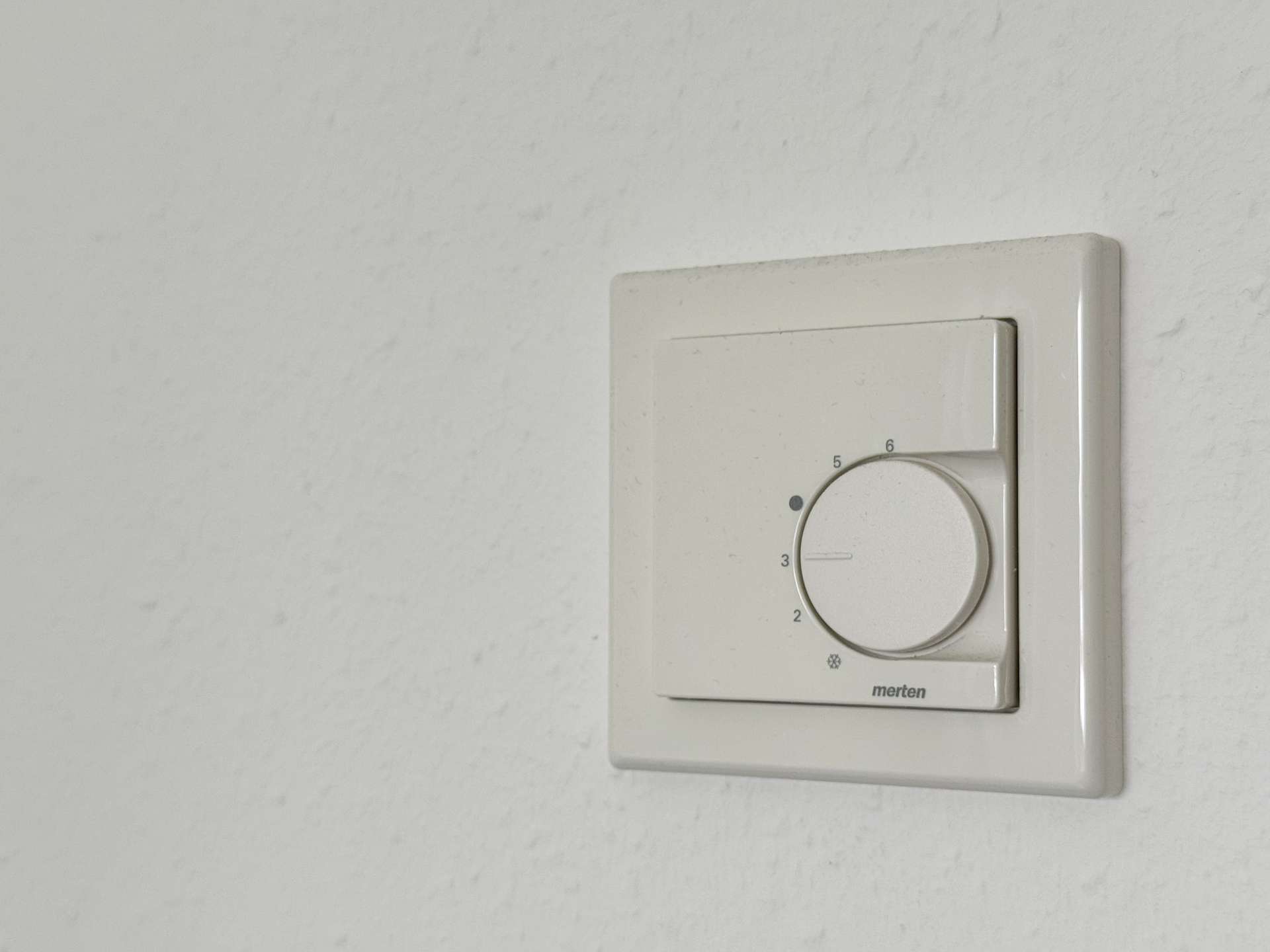 White wall-mounted thermostat with a circular dial set near 4, mounted on a pale wall
