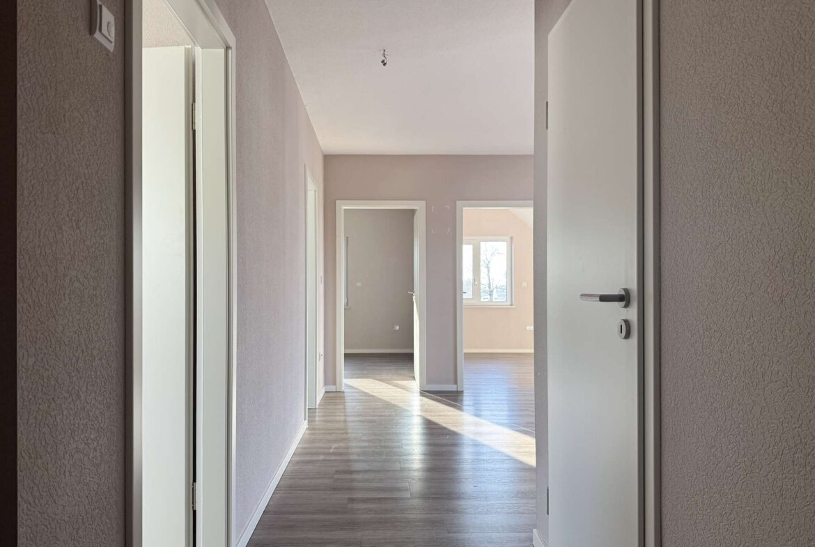 Bright hallway in a modern home with open doorways and a sunlit room at the far end.