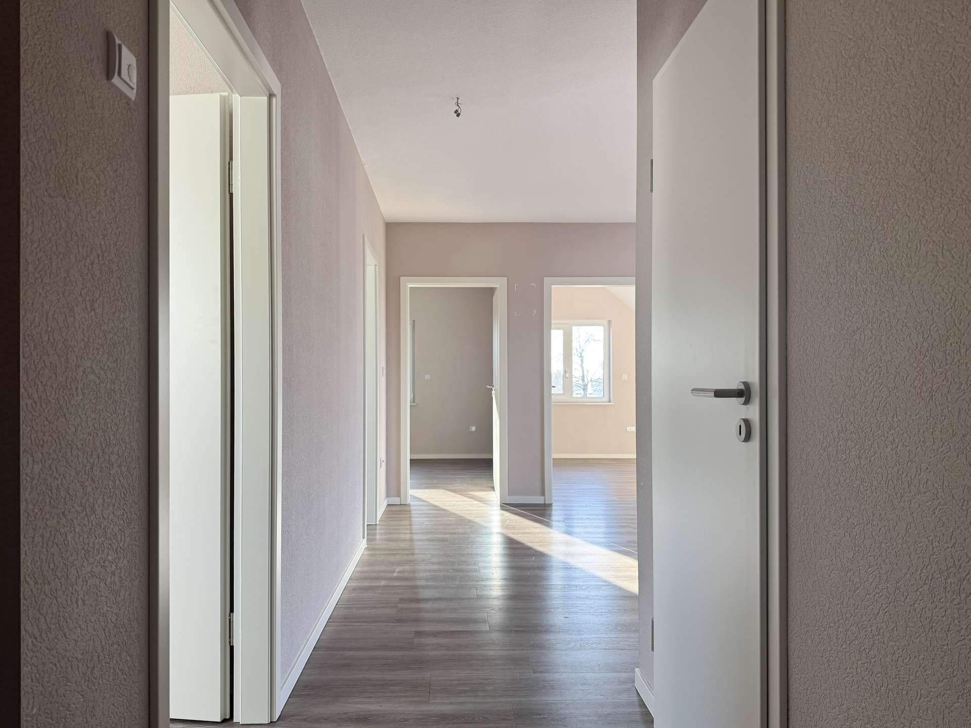 Bright hallway in a modern home with open doorways and a sunlit room at the far end.