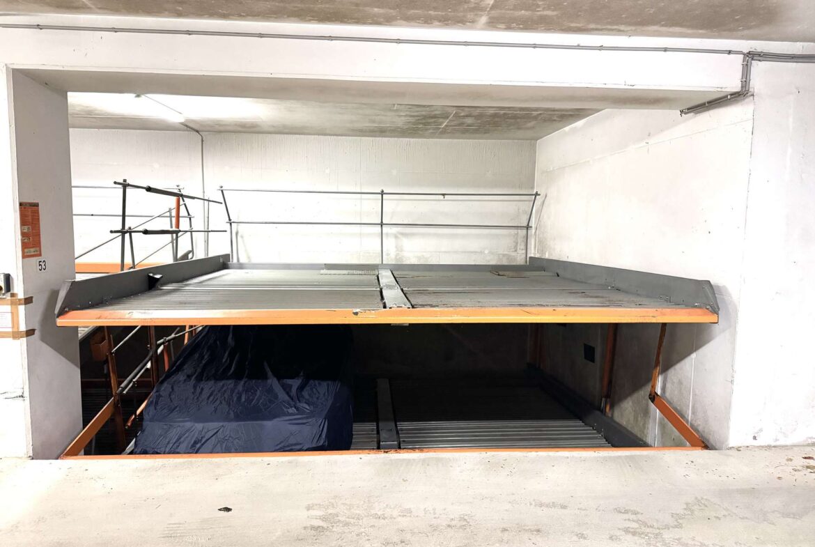 Industrial freight elevator platform with grated metal deck and orange edge rails in a white concrete loading area, scaffolding visible behind.
