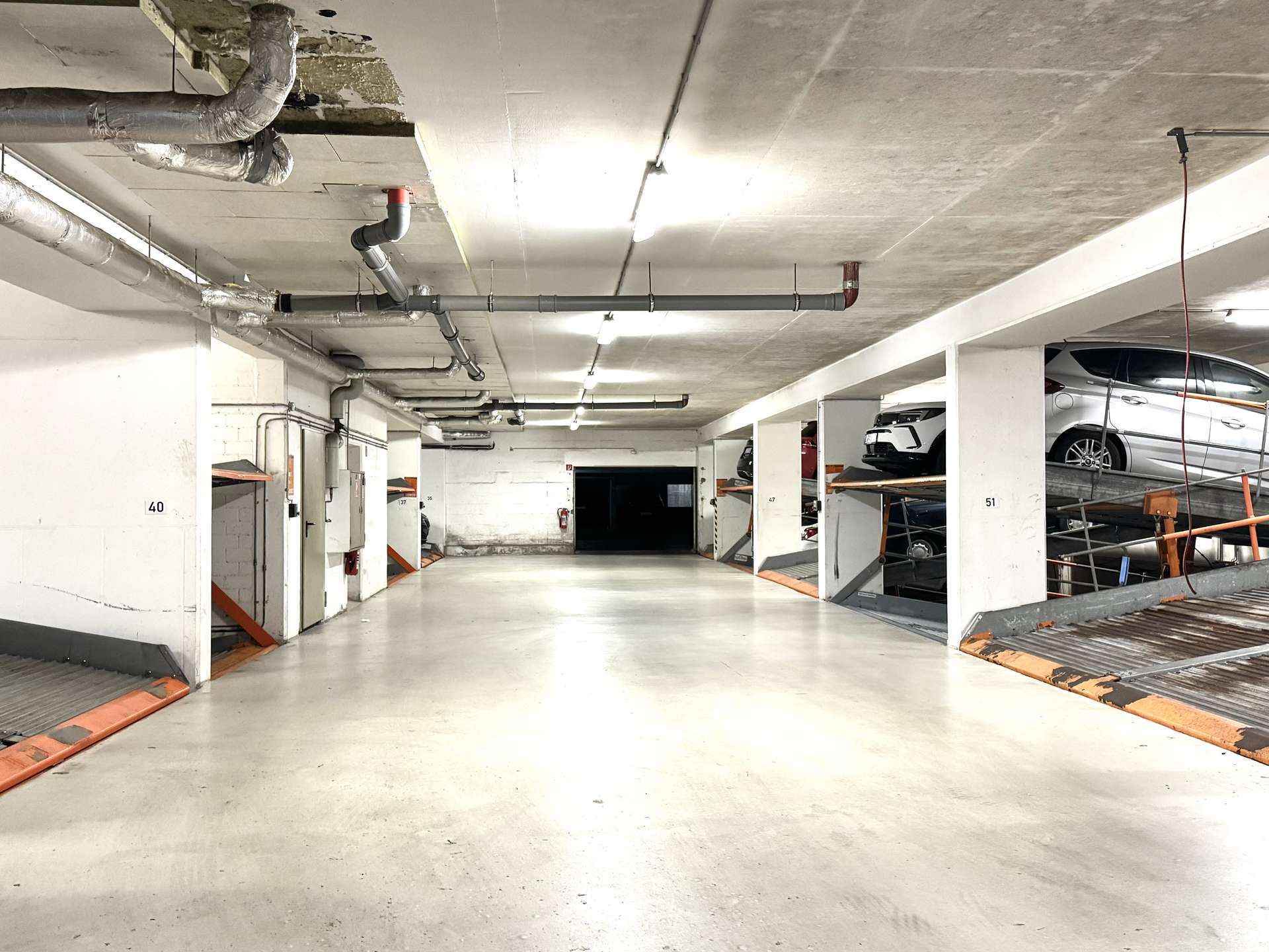 Underground parking garage corridor with stacked car bays on the right and exposed pipes along the ceiling.