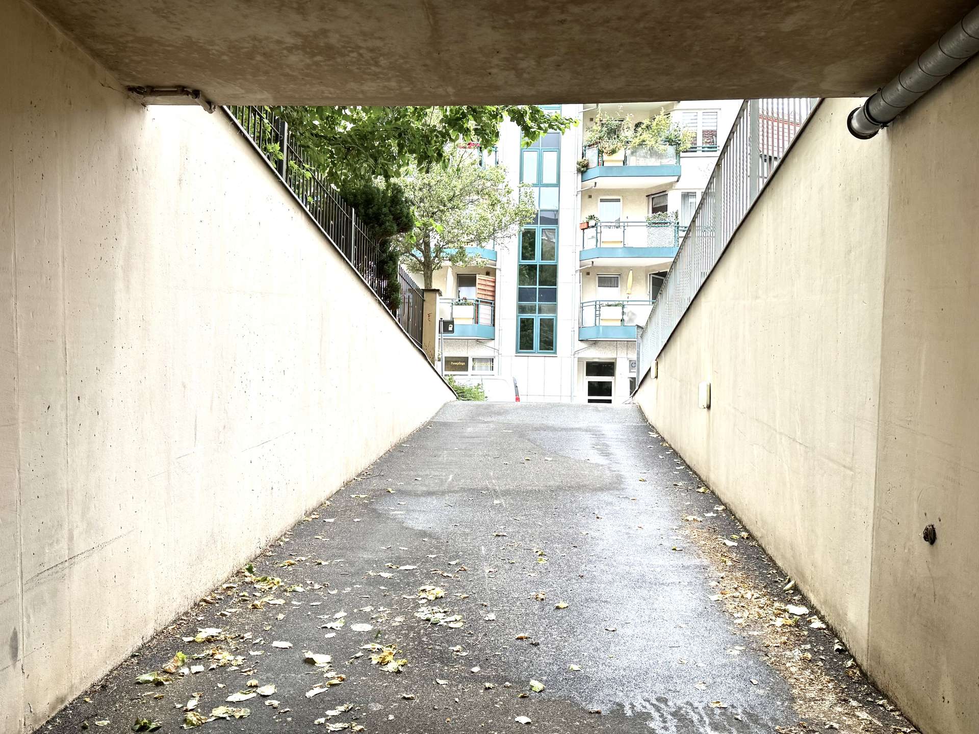 Underground pedestrian tunnel opening to a street with apartment buildings, trees, and scattered fallen leaves on the pavement.