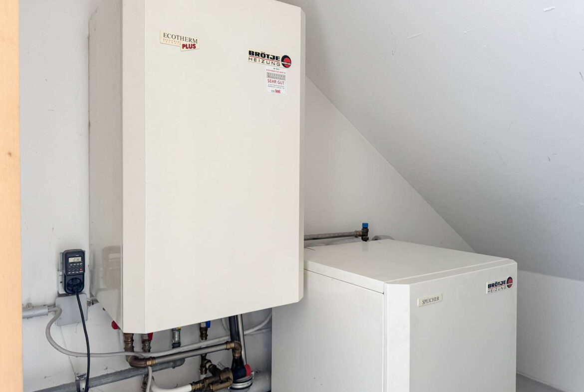 White utility cabinet and boiler unit mounted on a light wall, with exposed pipes and a small control box to the left side of the frame.