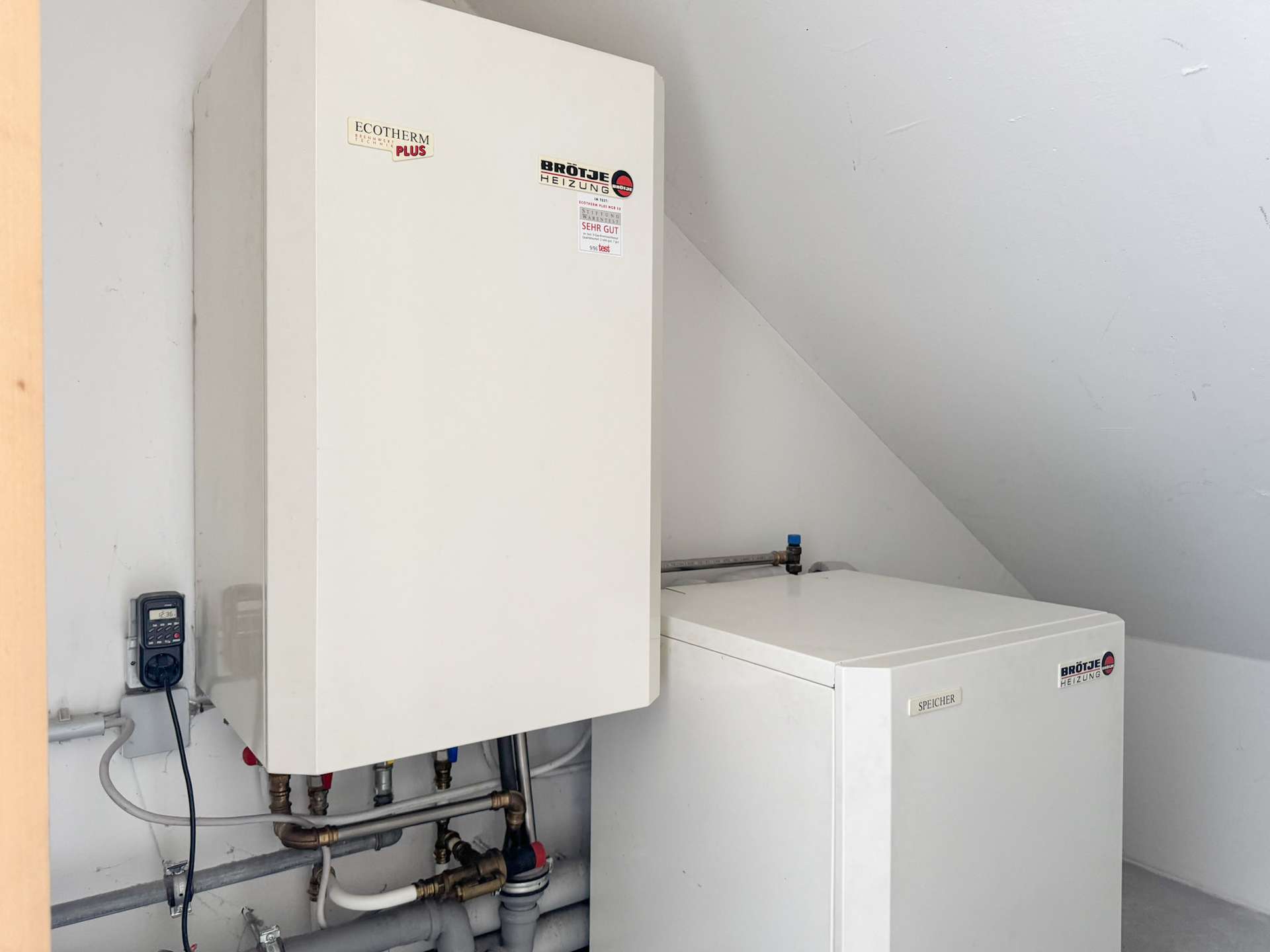 White utility cabinet and boiler unit mounted on a light wall, with exposed pipes and a small control box to the left side of the frame.