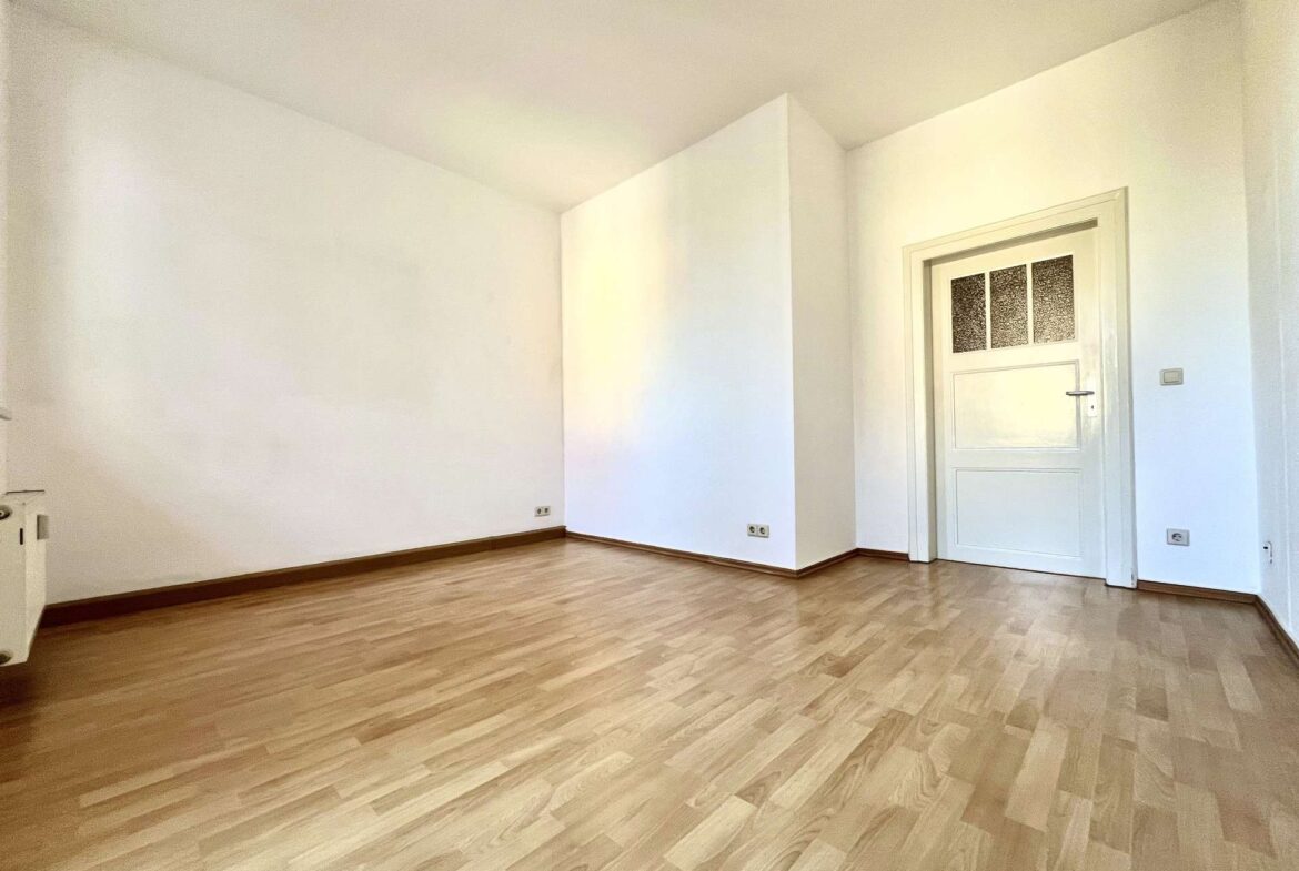 Bright empty room with light wood floor, white walls, and a white door with frosted glass panels on the right.