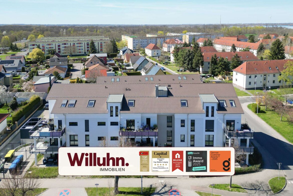 Aerial view of a suburban neighborhood with white apartment buildings; foreground shows a large Willuhn Immobilien sign.