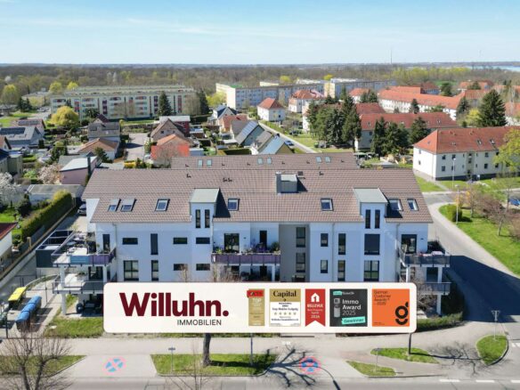 Aerial view of a suburban neighborhood with white apartment buildings; foreground shows a large Willuhn Immobilien sign.