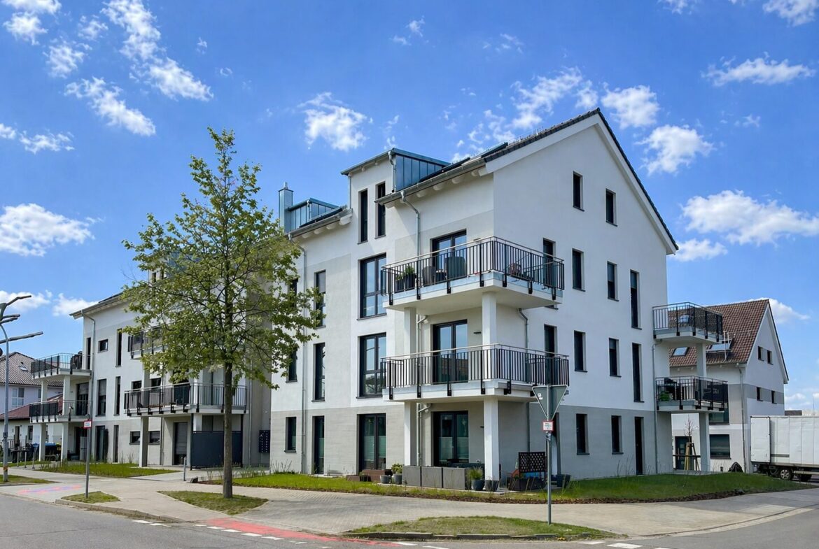 White modern apartment building with multiple balconies along a corner lot, blue sky above.