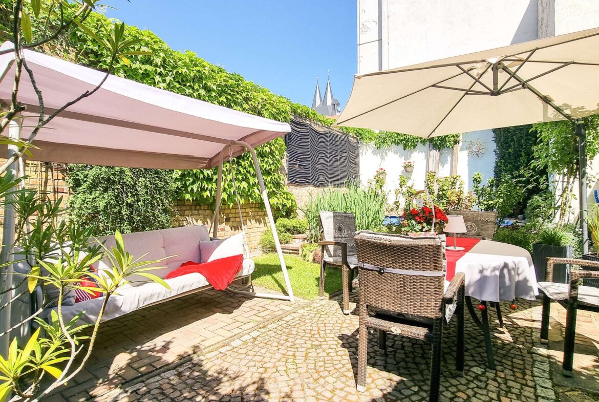 Outdoor patio with cushioned seating, wicker chairs, and large beige umbrellas on a sunny day.