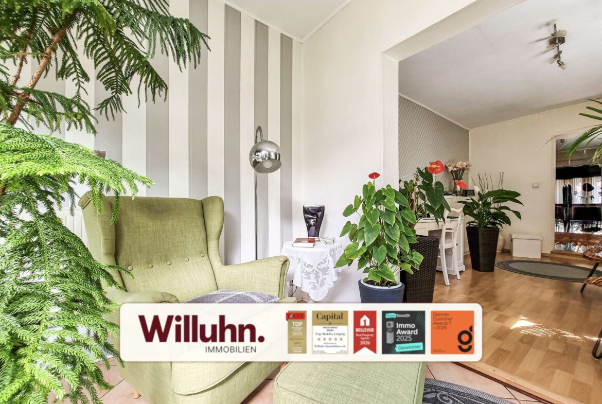 Bright living room with green upholstered armchairs, large leafy plants, and a vertical gray-and-white striped accent wall.