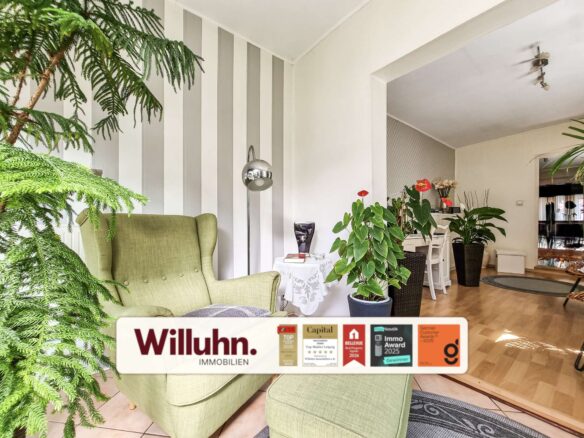 Bright living room with green upholstered armchairs, large leafy plants, and a vertical gray-and-white striped accent wall.