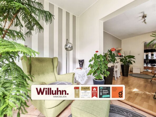 Bright living room with green upholstered armchairs, large leafy plants, and a vertical gray-and-white striped accent wall.