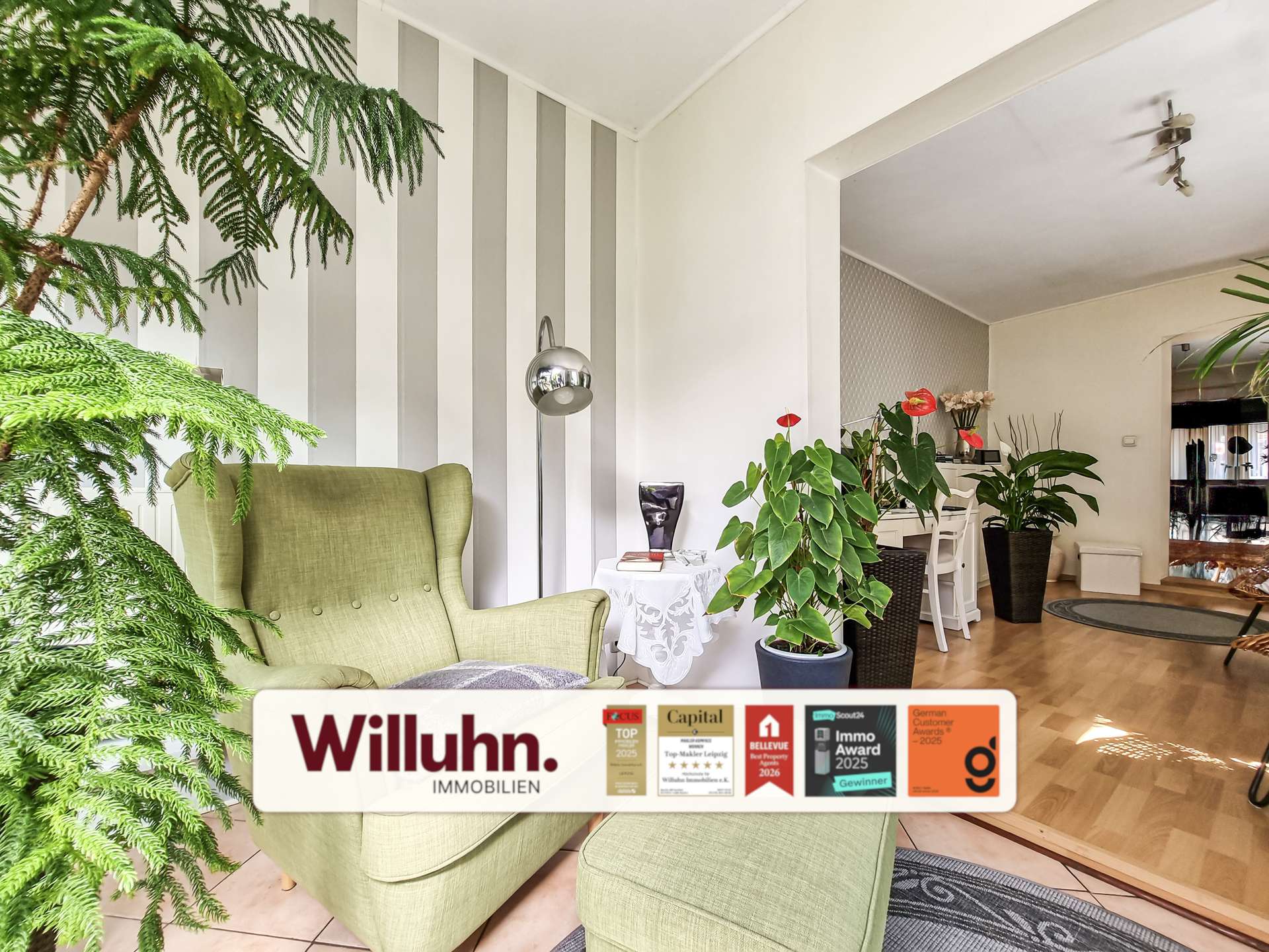 Bright living room with green upholstered armchairs, large leafy plants, and a vertical gray-and-white striped accent wall.