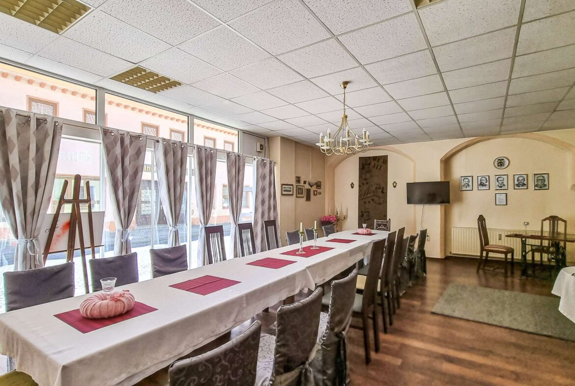 Banquet hall set for a formal meal: long white-clothed table with pink placemats and pumpkin centerpieces, gray chair covers.