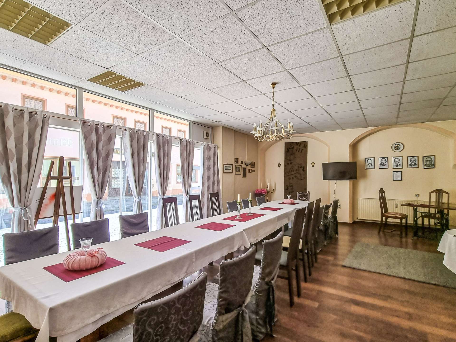 Banquet hall set for a formal meal: long white-clothed table with pink placemats and pumpkin centerpieces, gray chair covers.