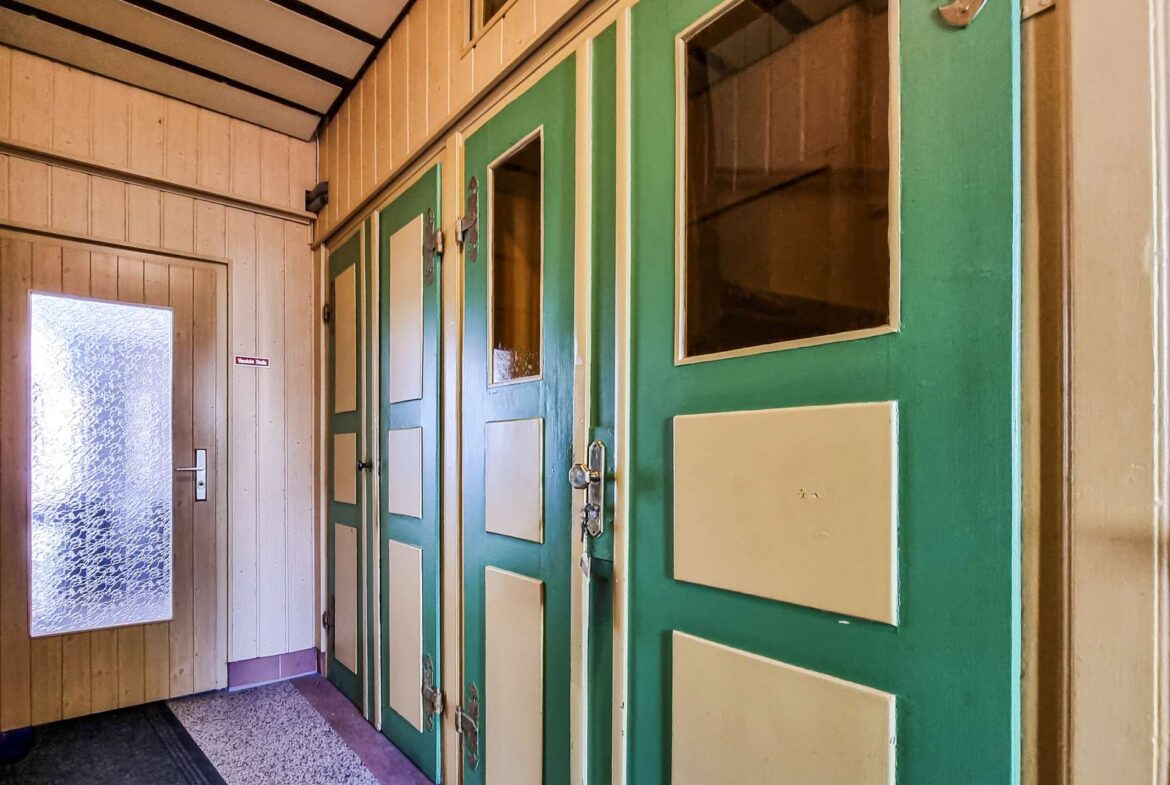 Indoor hallway with green doors featuring cream panels on the right and a frosted glass door at left.