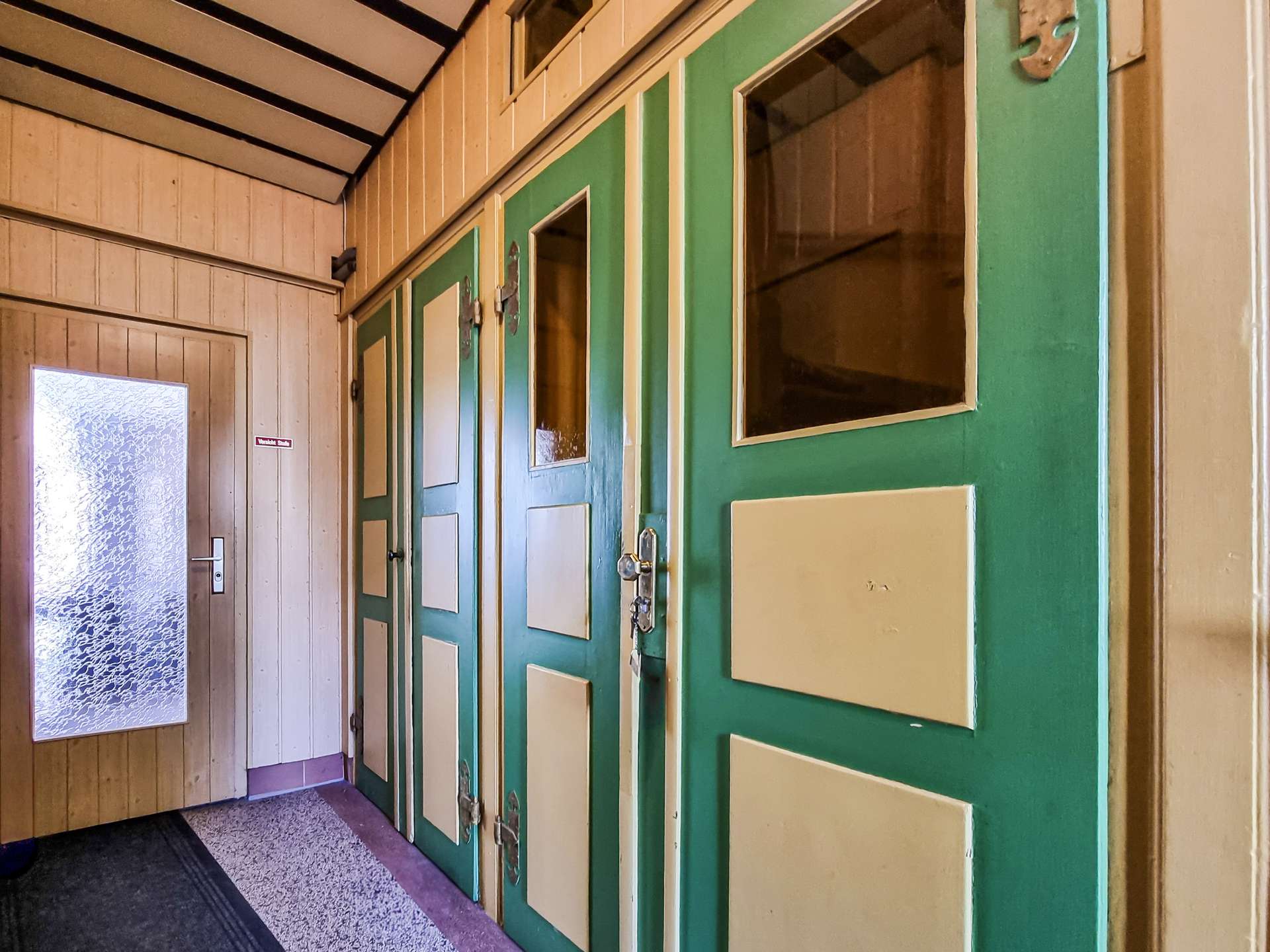 Indoor hallway with green doors featuring cream panels on the right and a frosted glass door at left.
