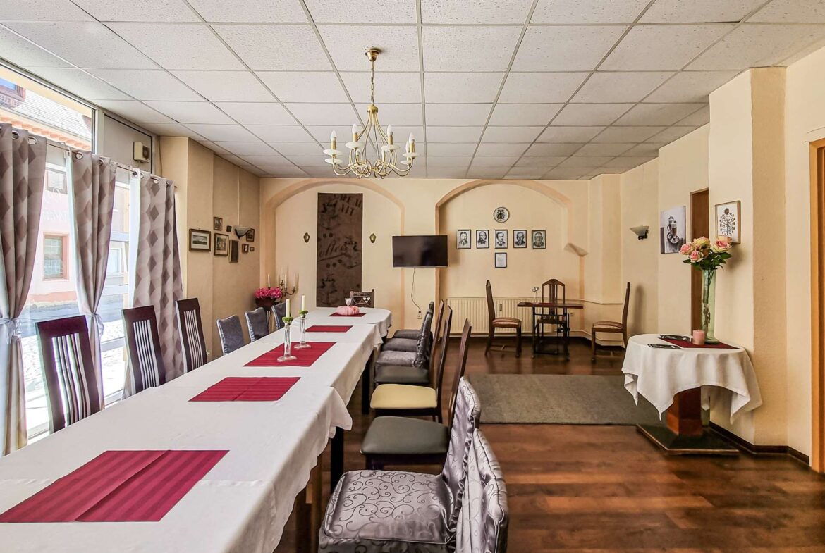 Banquet hall with a long white-draped table, pink runners, and a chandelier overhead in a softly lit room.