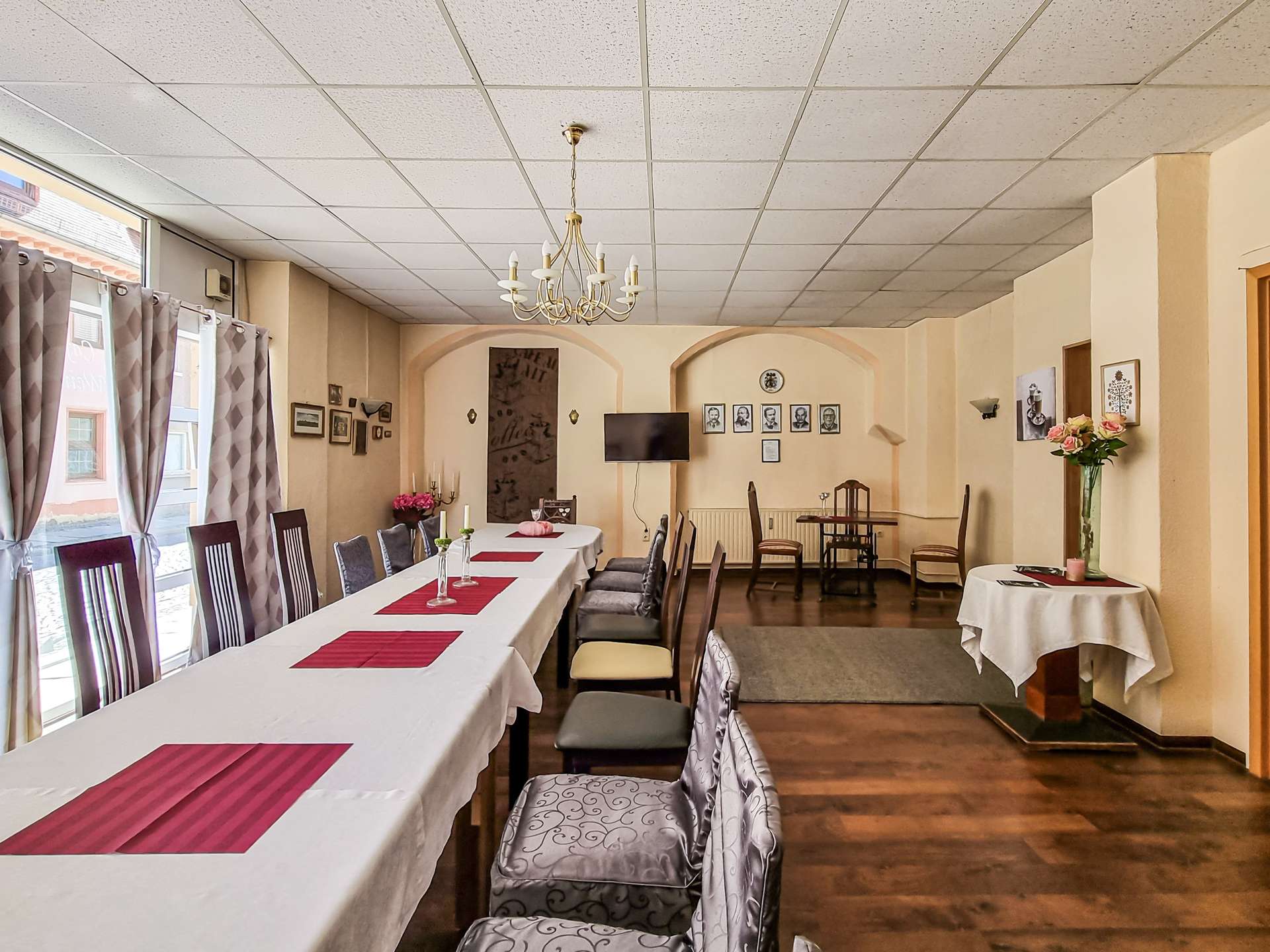 Banquet hall with a long white-draped table, pink runners, and a chandelier overhead in a softly lit room.