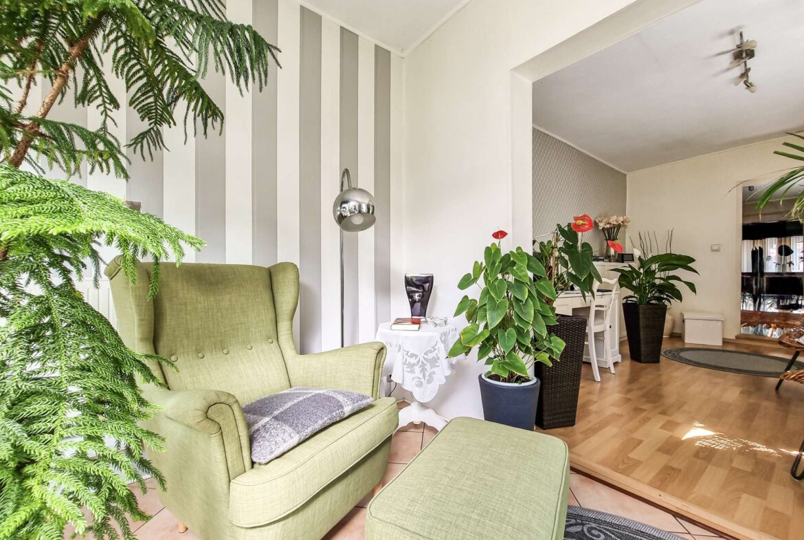 Bright living room with green upholstered chairs, large houseplants, and a striped wall behind.