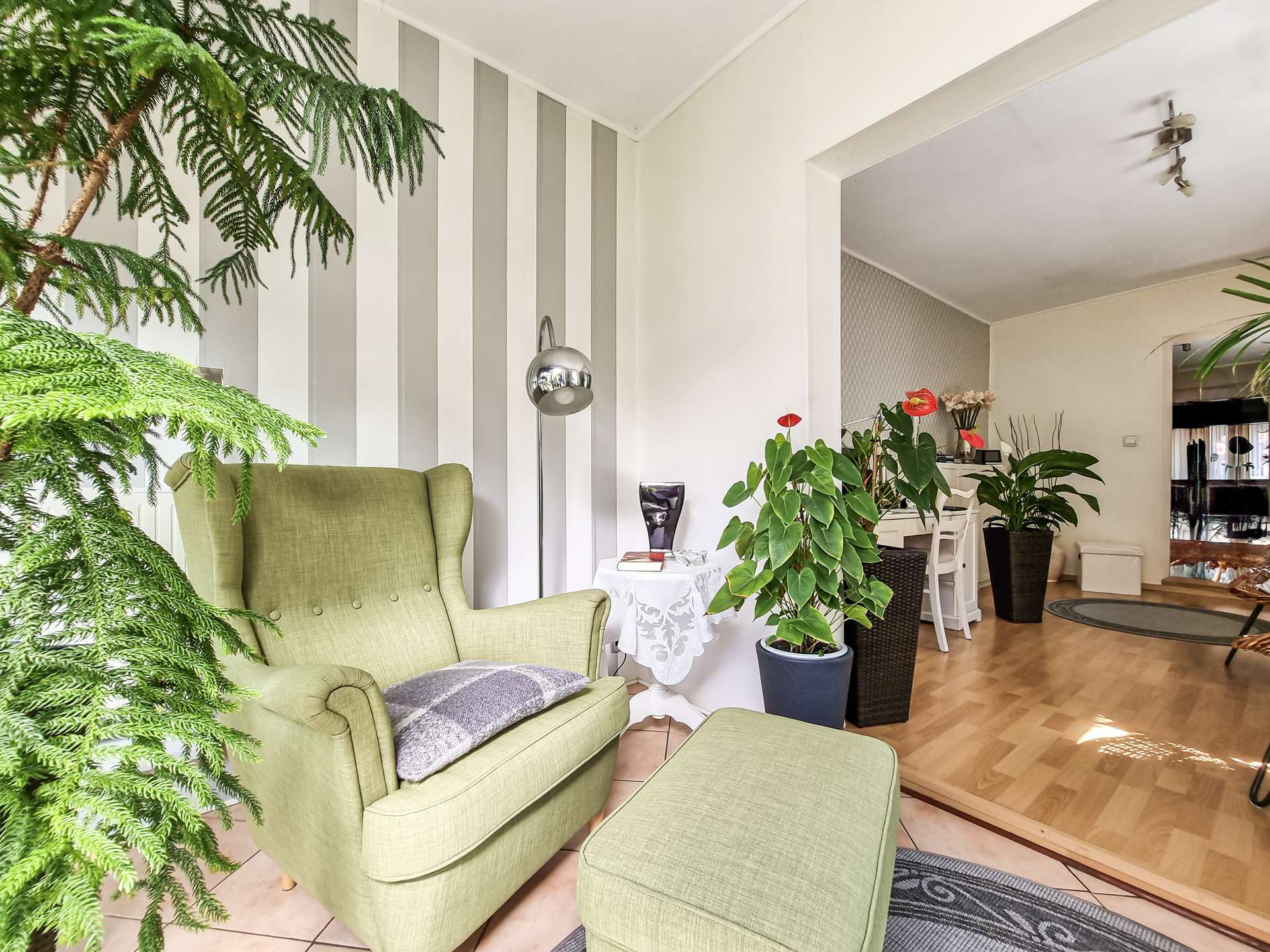 Bright living room with green upholstered chairs, large houseplants, and a striped wall behind.