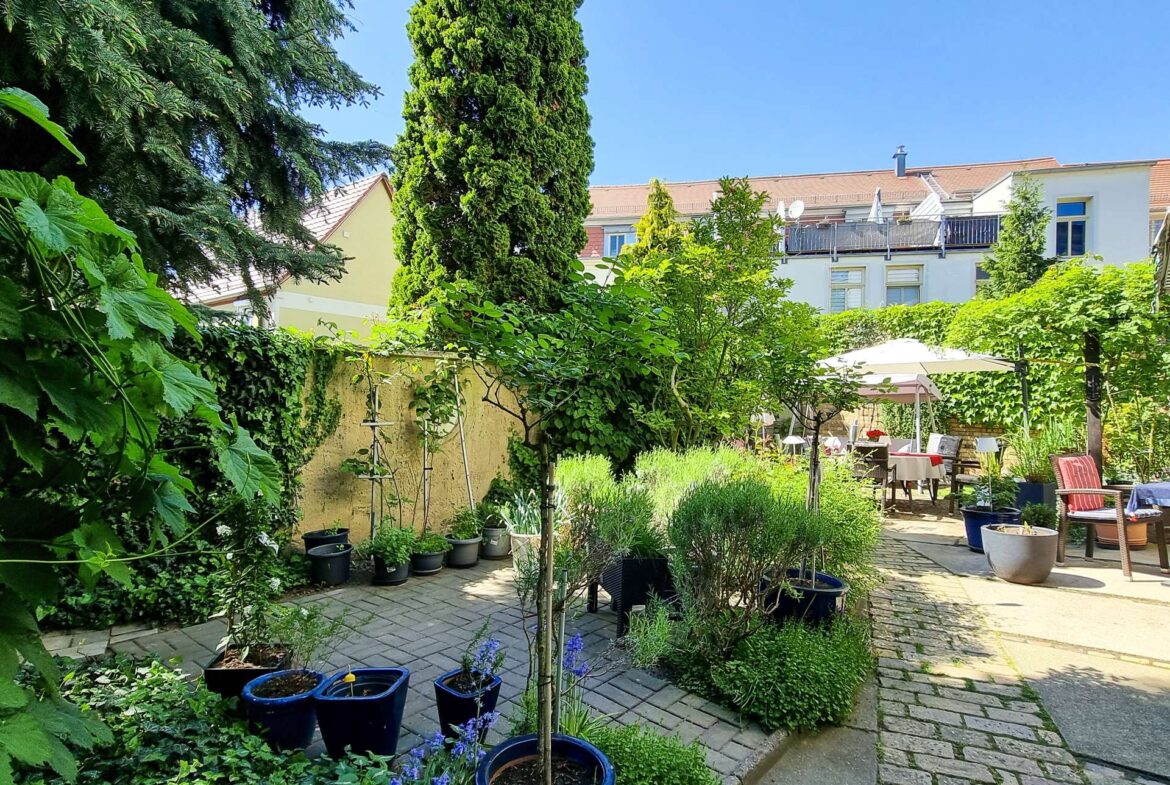 Lush urban backyard courtyard with potted trees and seating area; apartment buildings in the background.
