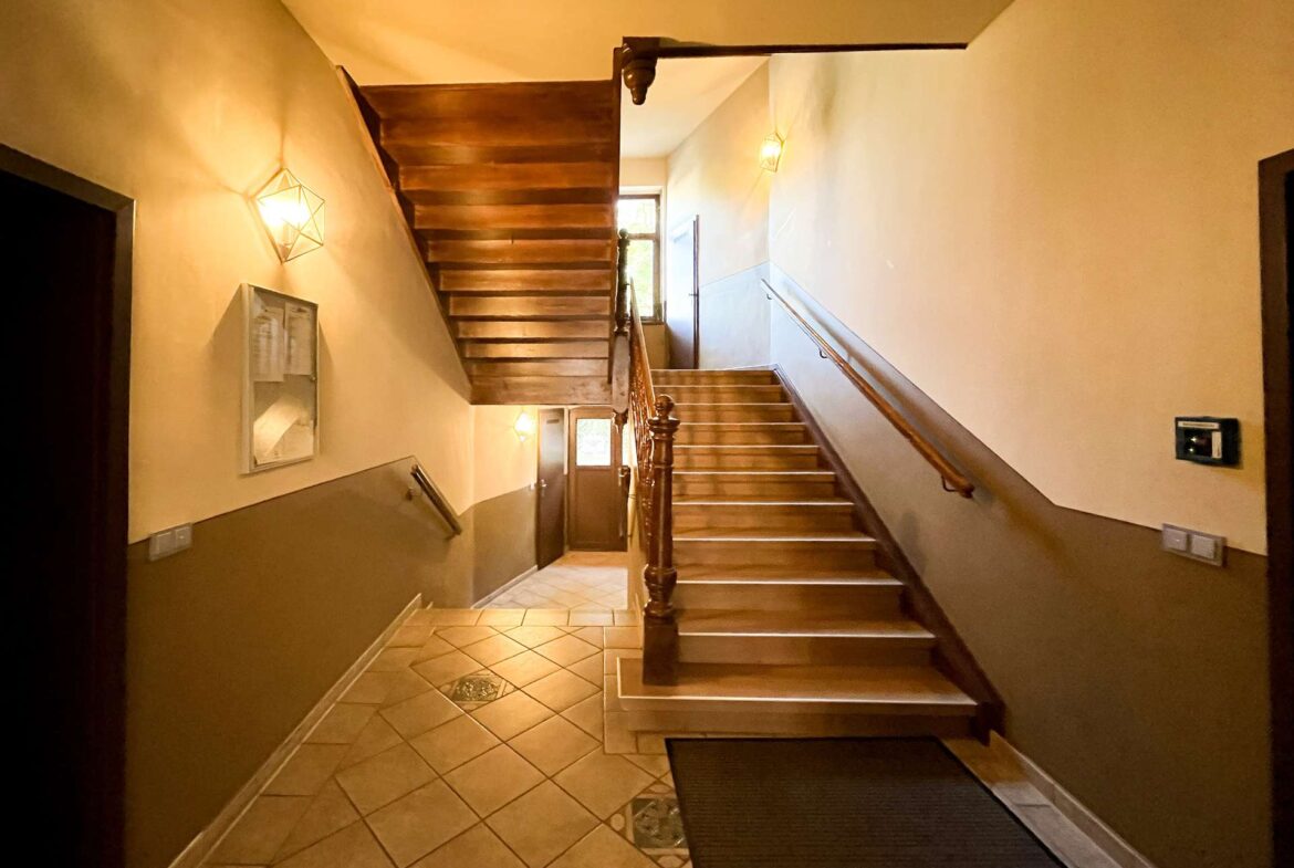 Interior stairwell with a polished wooden staircase, brown walls, and warm wall sconces lighting the hallway