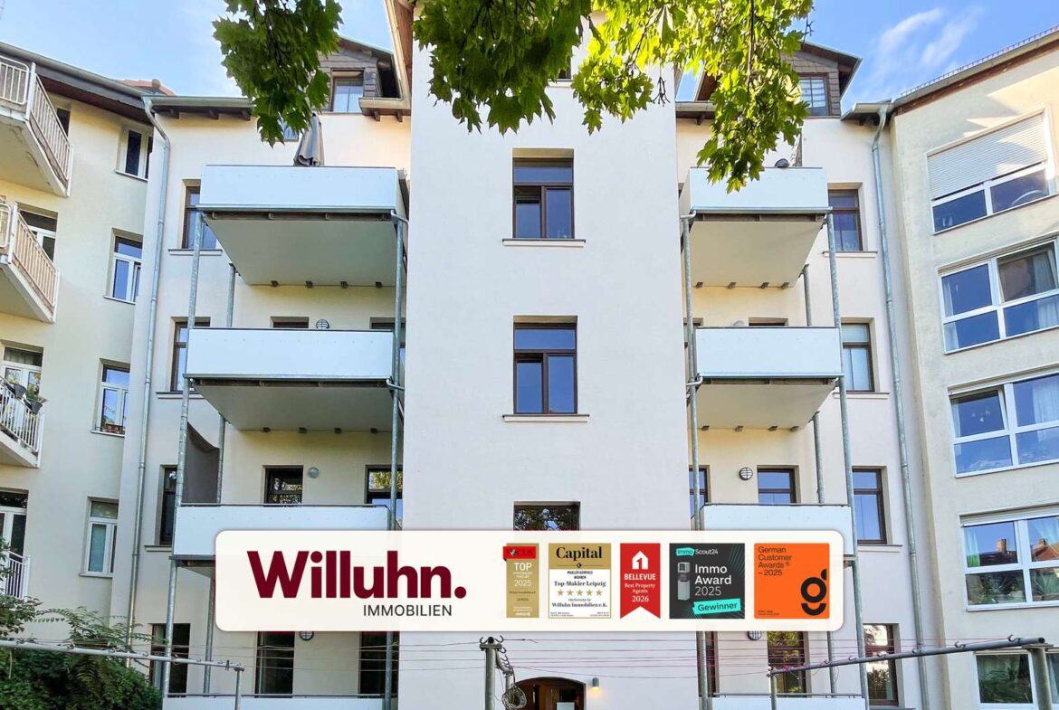 Modern residential building with balconies and a large Willuhn Immobilien sign in front, advertising awards and badges.