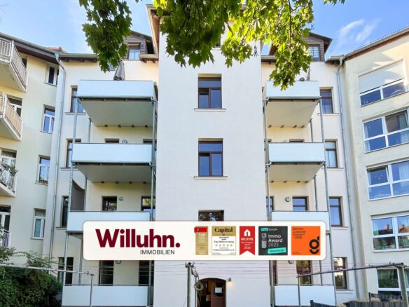 Modern residential building with balconies and a large Willuhn Immobilien sign in front, advertising awards and badges.