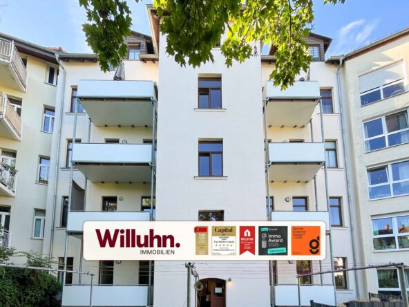 Modern residential building with balconies and a large Willuhn Immobilien sign in front, advertising awards and badges.