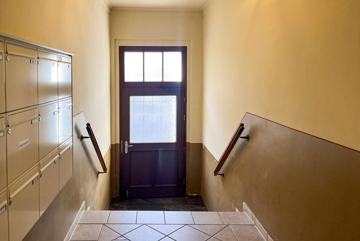 Narrow apartment hallway with beige walls, a row of mailboxes on the left, and a dark front door at the far end.