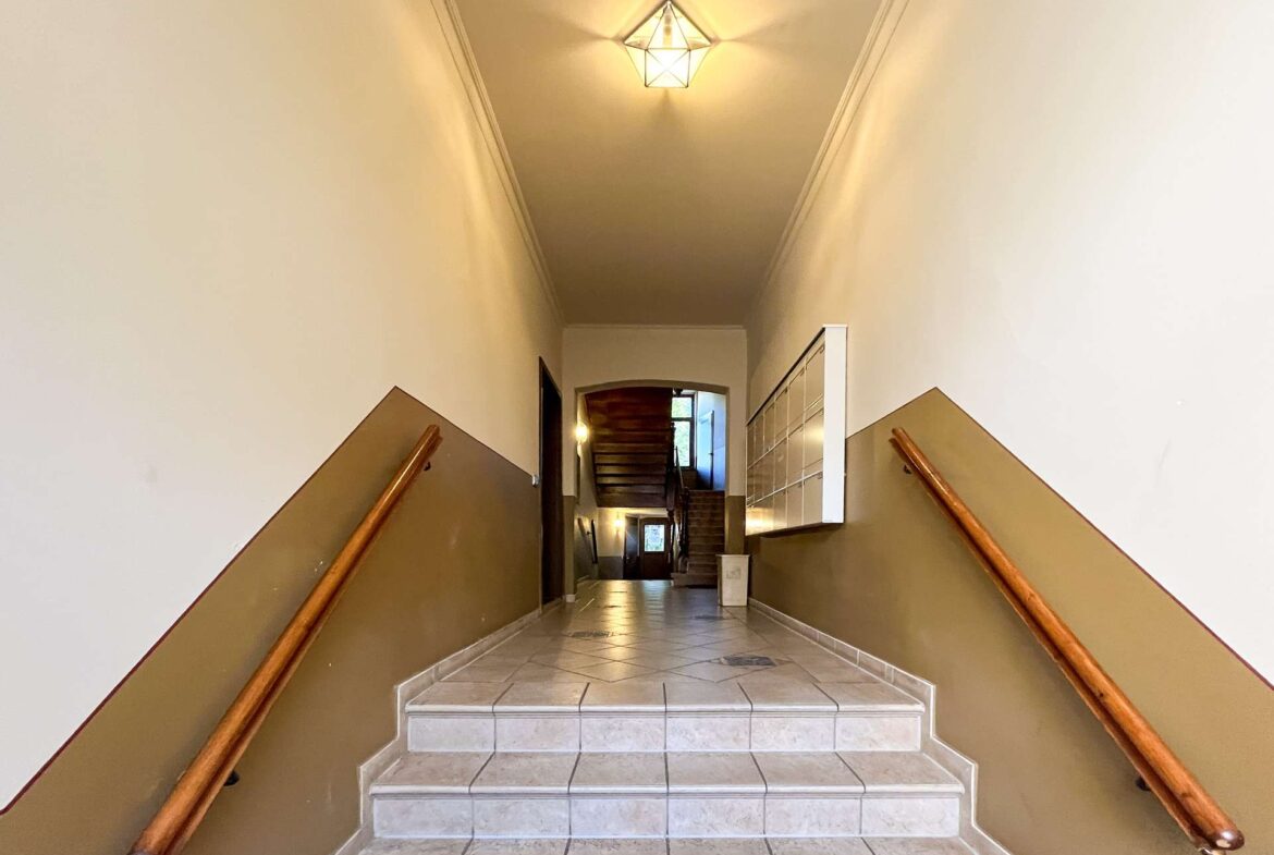 Interior stairwell with tiled steps, brown walls, and wooden handrails on both sides leading to a doorway at the top.