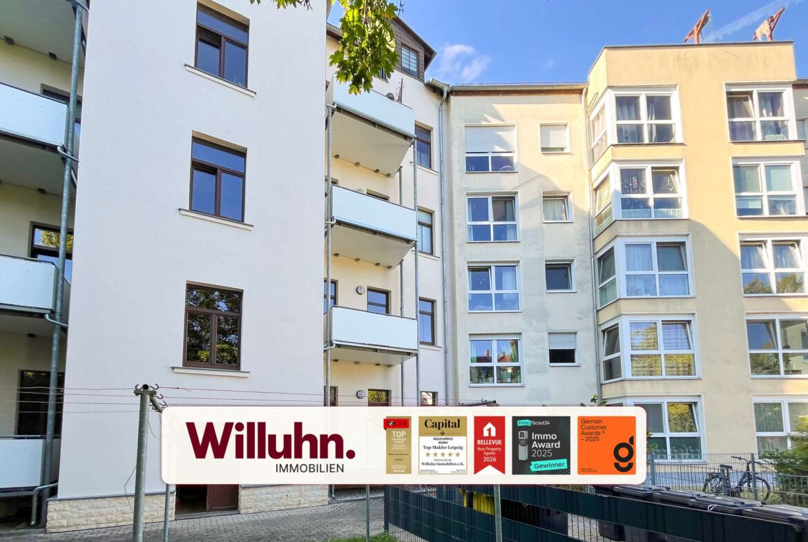 White and beige apartment building with balconies and large Willuhn Immobilien banner at ground level, displaying award logos