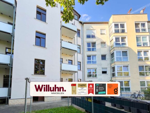 White and beige apartment building with balconies and large Willuhn Immobilien banner at ground level, displaying award logos