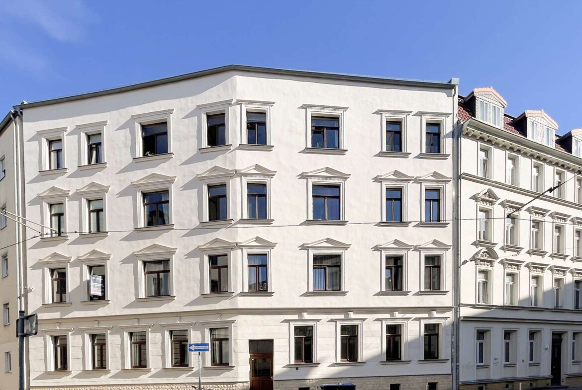 White, multi-story building with decorative window frames against a clear blue sky, street view with a bicycle nearby