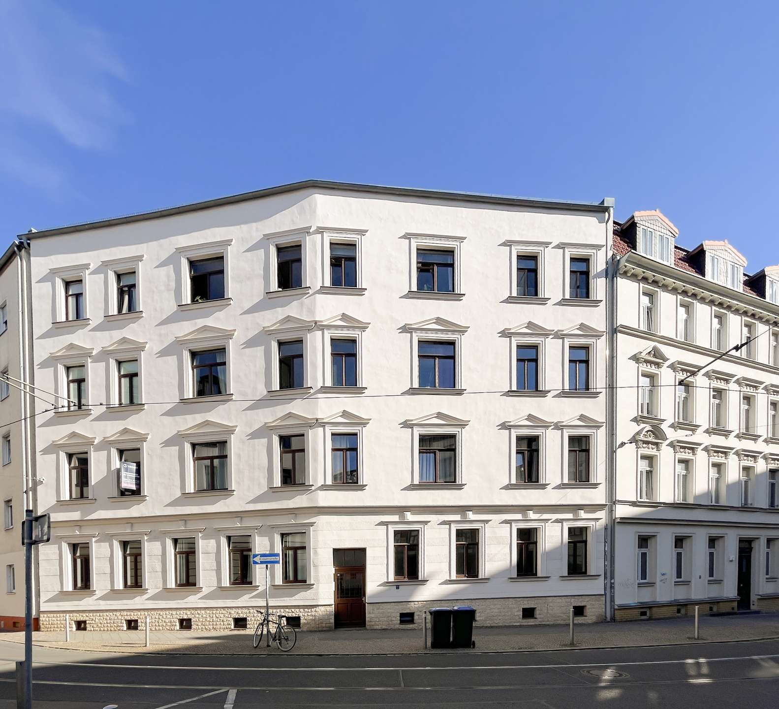 White, multi-story building with decorative window frames against a clear blue sky, street view with a bicycle nearby