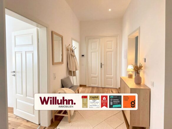 Bright entry hallway with white doors, a coat rack and bench along the left wall, and a wooden console with a vase on the right; a Willuhn Immobilien banner at the bottom.