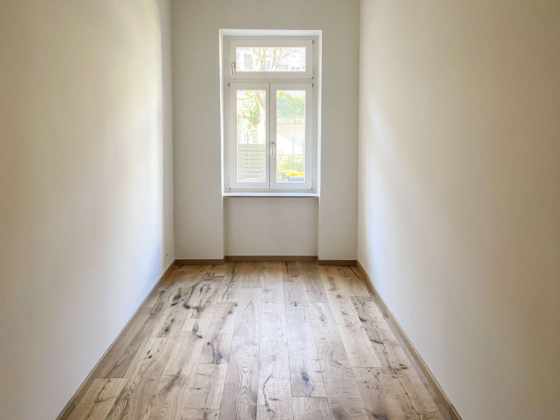Narrow hallway with light beige walls leading to a white-framed window at the far end; wooden floor visible.
