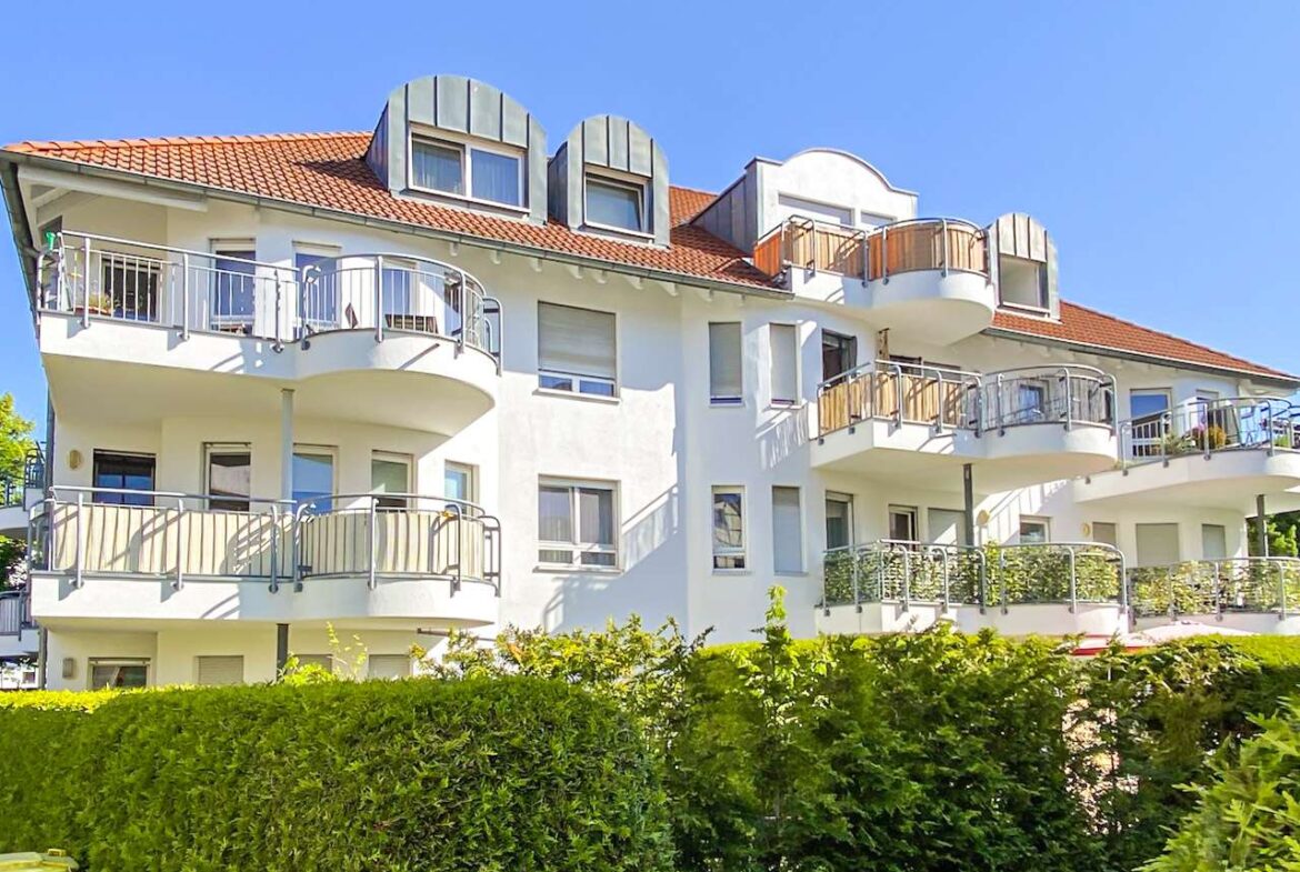 White modern apartment building with curved balconies, red-tiled roof, and a blue sky above.