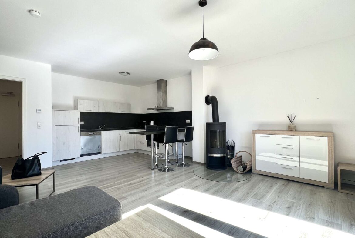 Open-plan kitchen and living area with white cabinets, black backsplash, and a central island with chrome bar stools.